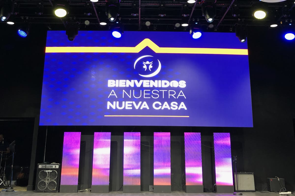 The LED wall on a stage showing a blue welcome graphic, lit by overhead moving lights, with a row of narrow LED columns along the stage front.
