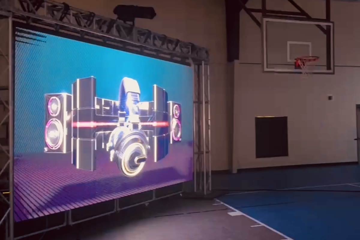 The LED wall standing in a ground-supported truss frame in an empty gymnasium, showing a bright graphic of loudspeakers and a turntable.